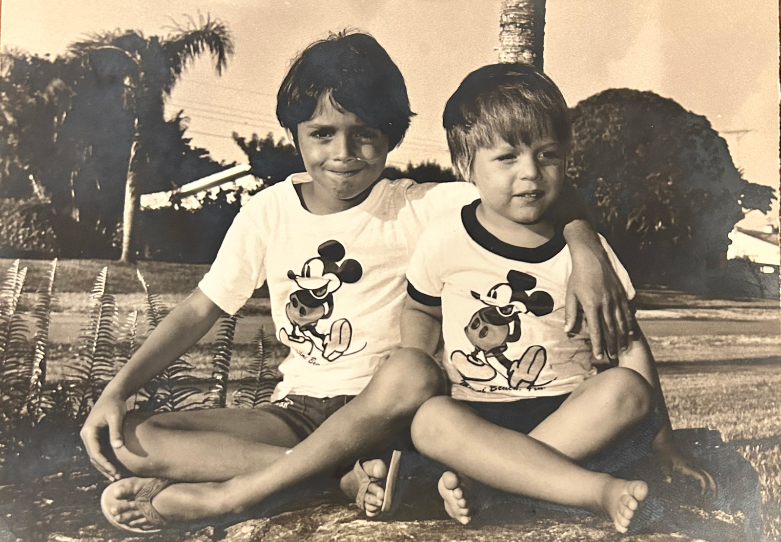 Two young boys in Mickey Mouse t-shirts sitting outside